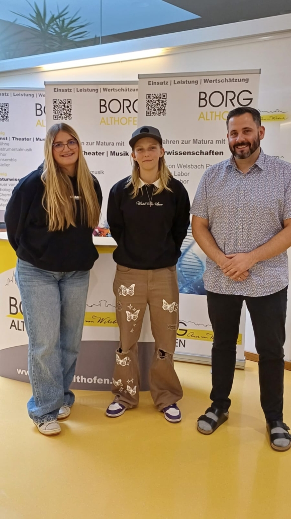Drei Personen vor BORG Althofen Banner: zwei junge Frauen, ein Mann.